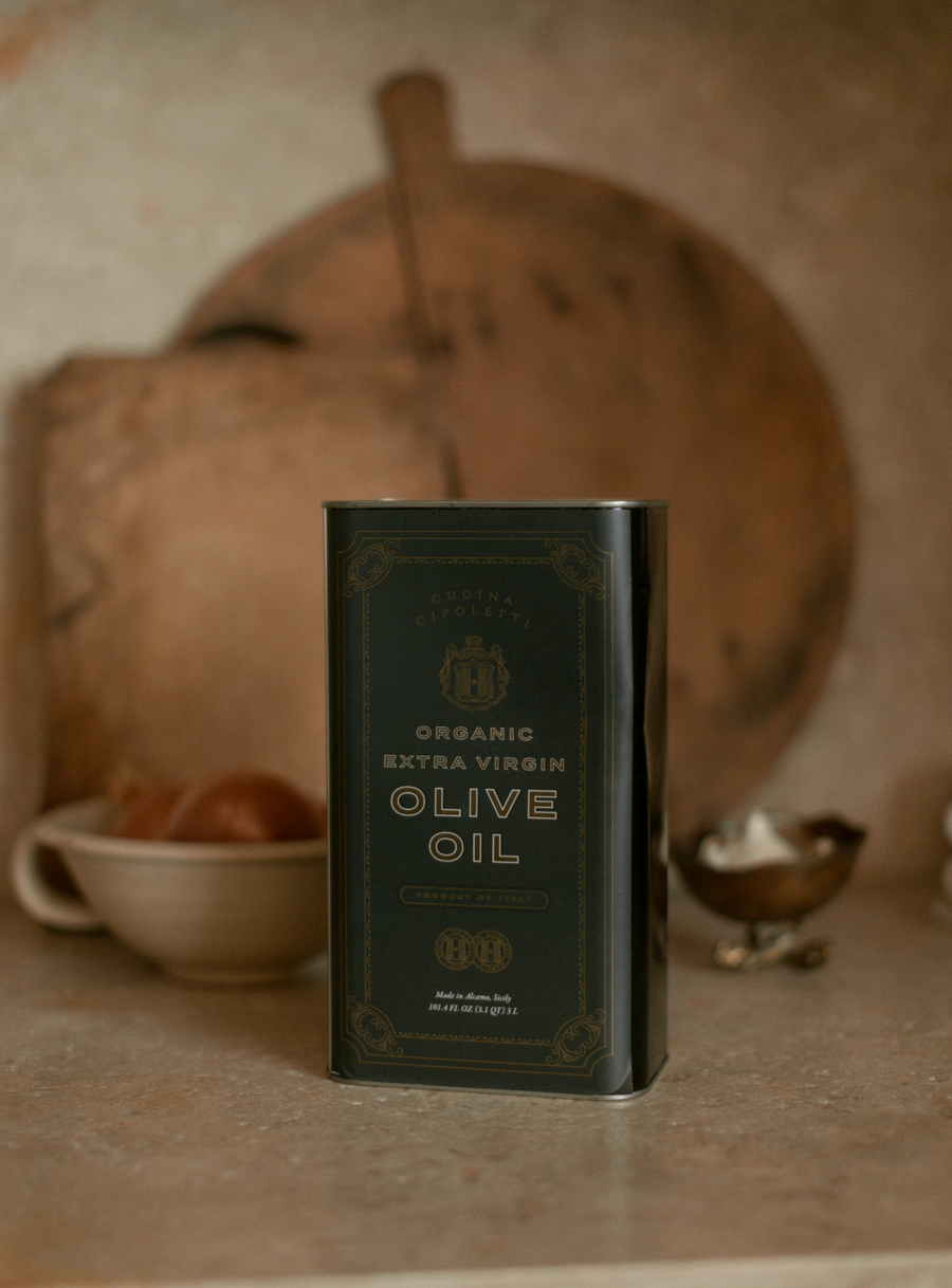 A tin container of Cucina Cipoletti Organic Extra Virgin Olive Oil placed on a kitchen counter with vintage kitchen tools in the background.