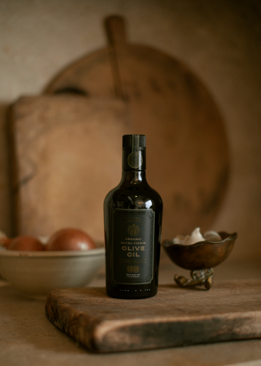 A bottle of organic extra virgin olive oil on a wooden surface, with a dark label and a cork top.